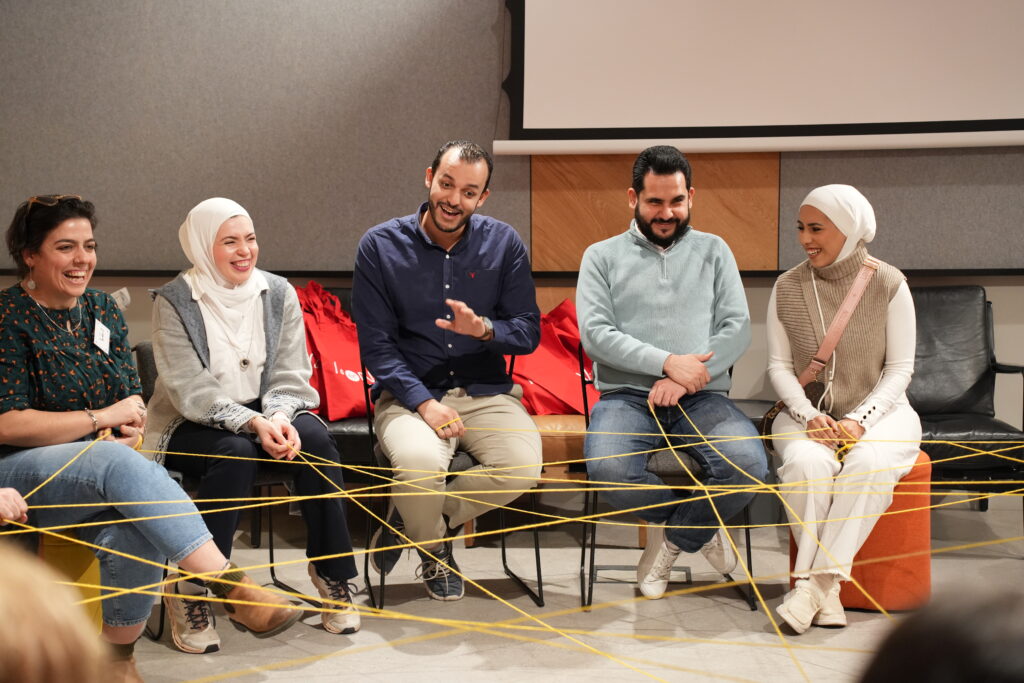 Group of five men and women sat in a circle laughing and smiling