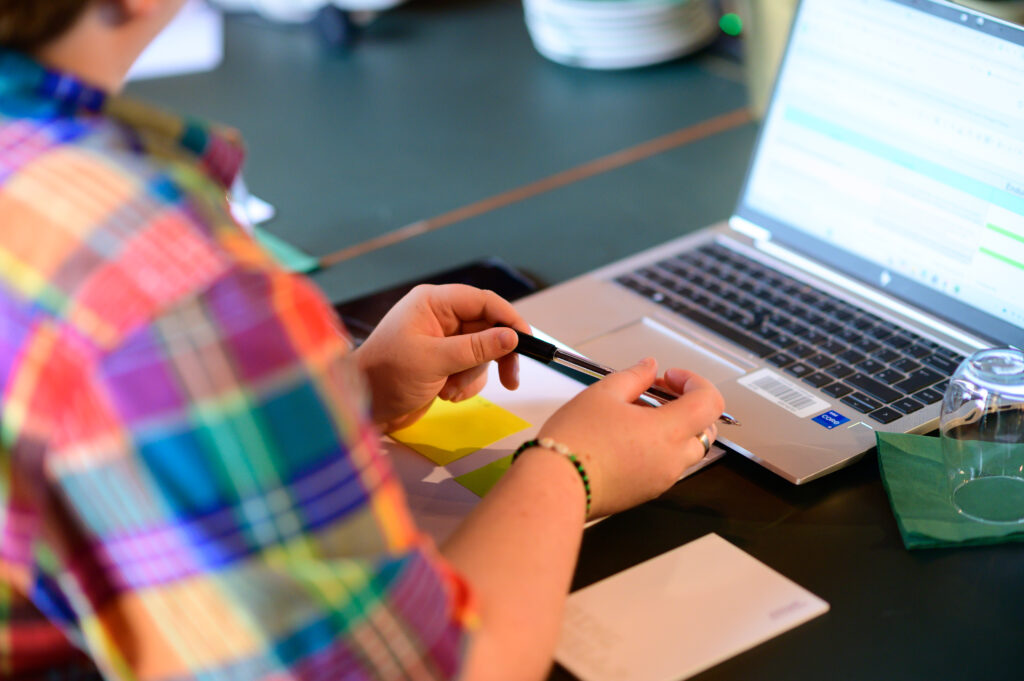 person sat at a laptop with pen in hand