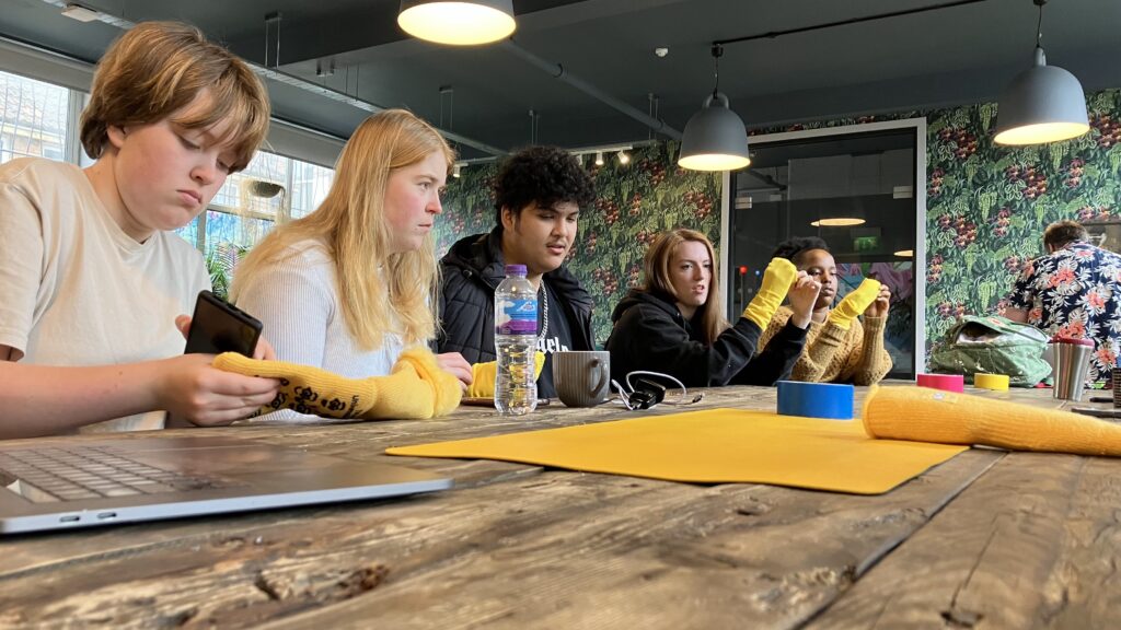 A group of young people with yellow sock puppets reflecting on their involvement in Lonely Not Alone since we launched in 2019