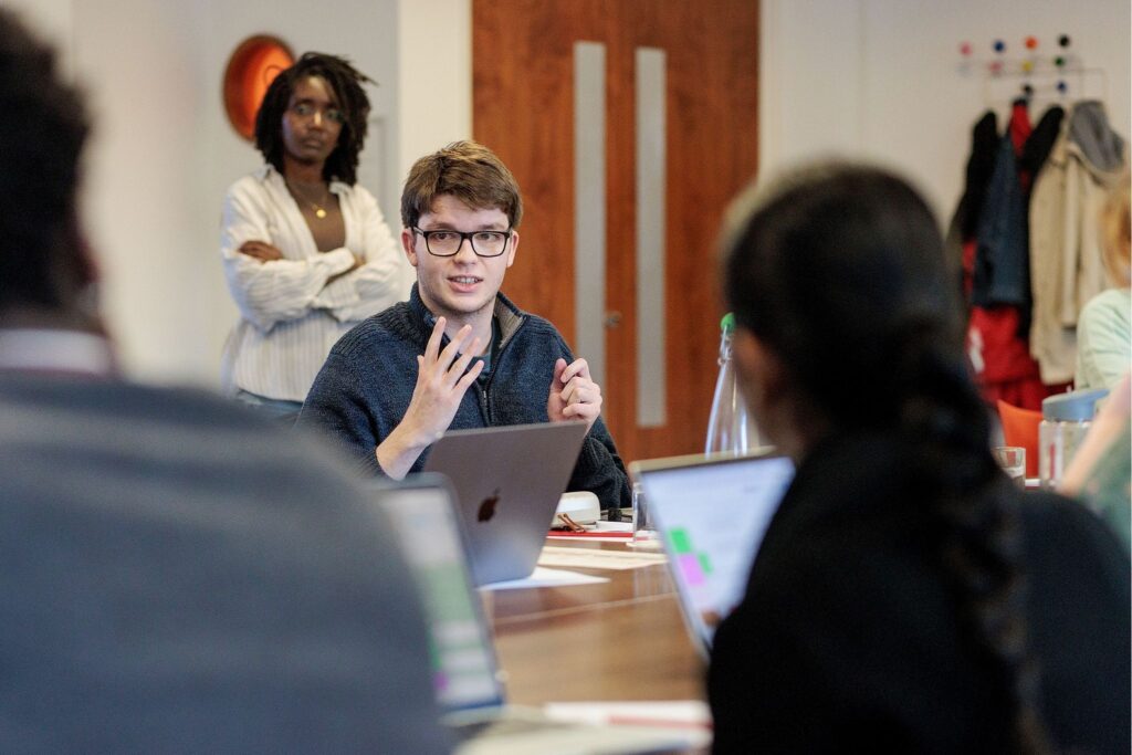 A person is sitting at a table and speaking animatedly to a group.