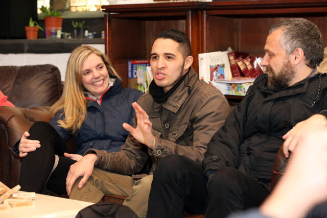 A woman and two men sat together. The woman on the end and the man on the end are both looking at the man in the centre who is explaining something