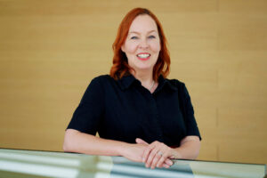 Portrait of Adele Balmforth, trustee of Co-op Foundation. Image shows head and shoulders of white woman with red hair wearing a dark blue shirt 