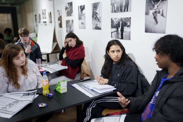 Young people sitting around a desk, talking. 