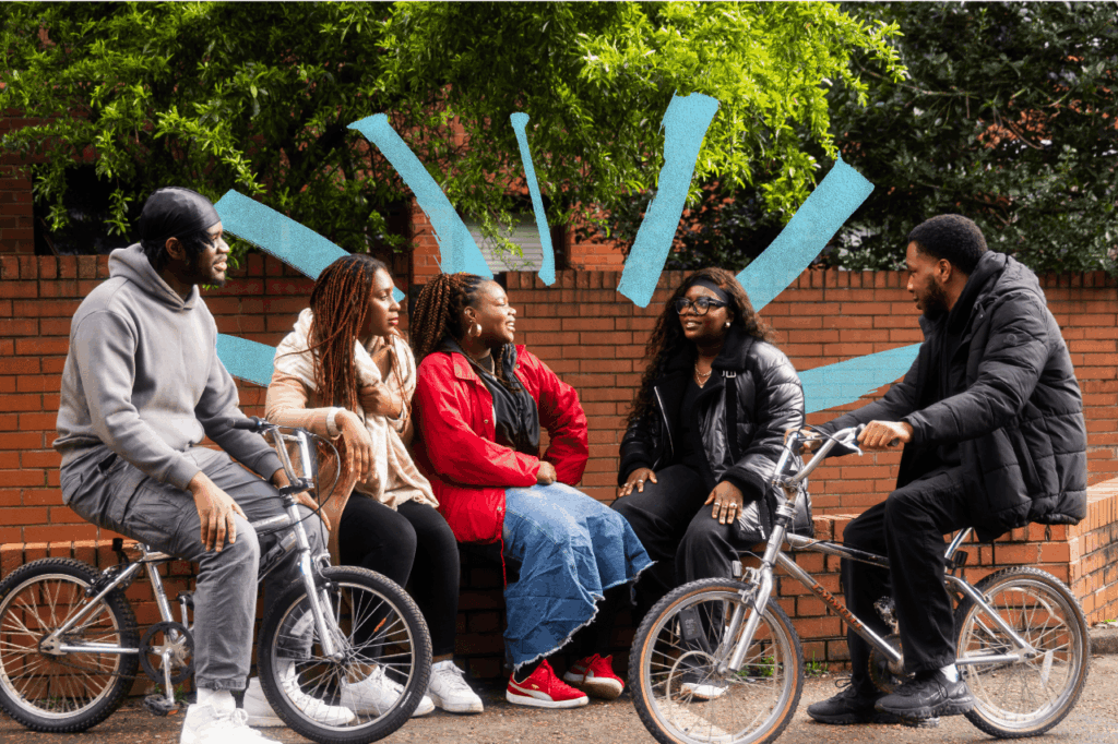 Group of young people sat outside, two are sat on bikes