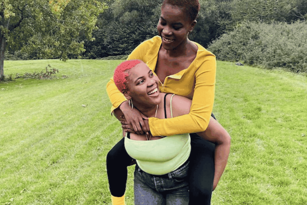 A young person giving another young person a piggy back and smiling at each other.