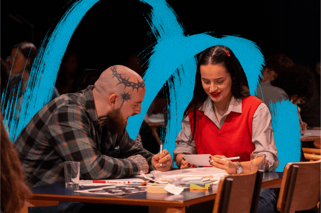 Young man and young woman sat at table, writing and smiling